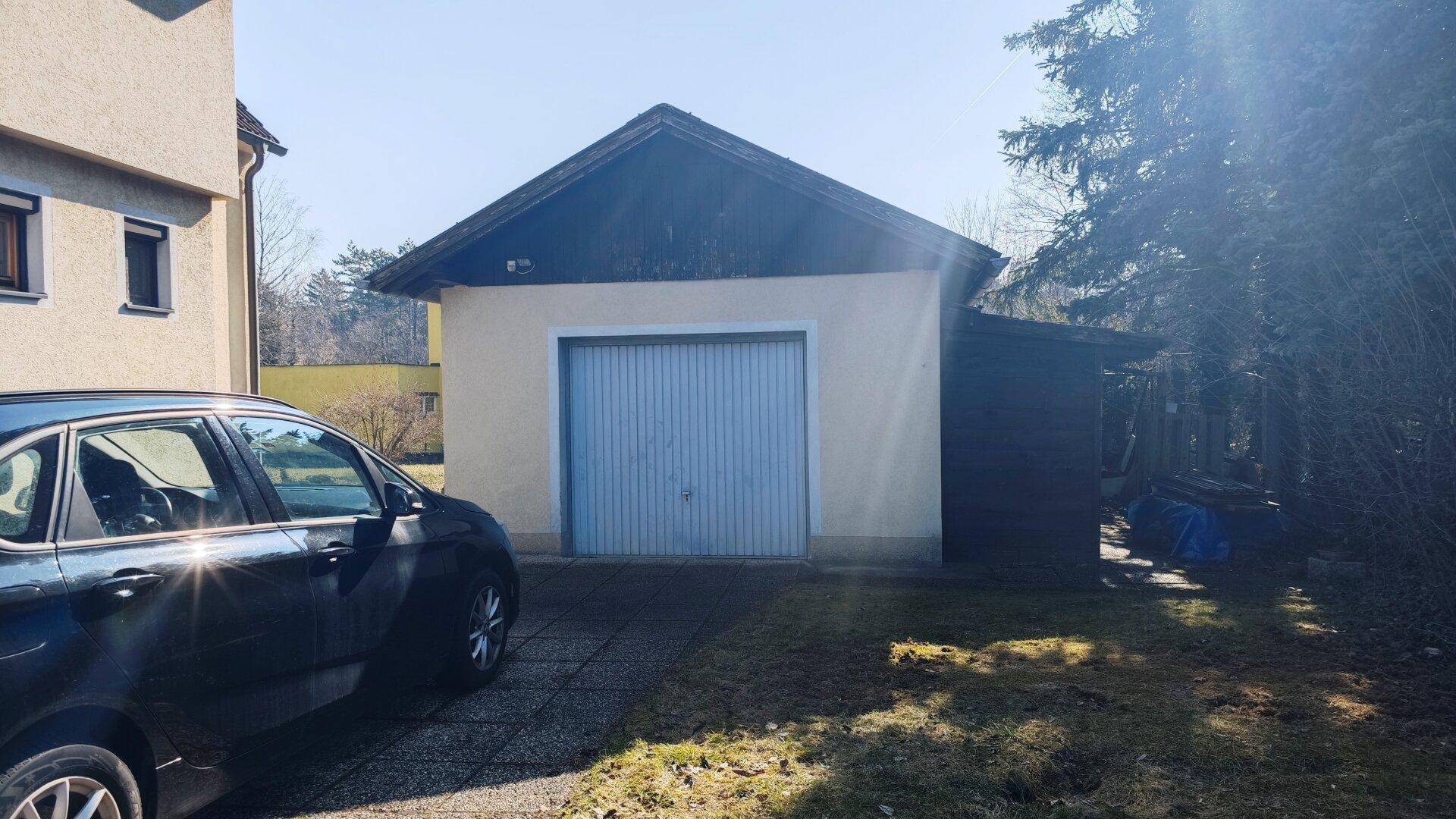 Einzelgarage mit blauem Tor und angrenzendem Carport, davor ein geparktes Auto.