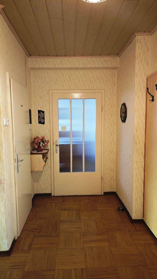 Heller Flur mit gemusterter Tapete, Holzdecke und einer Tür mit Glaseinsätzen.