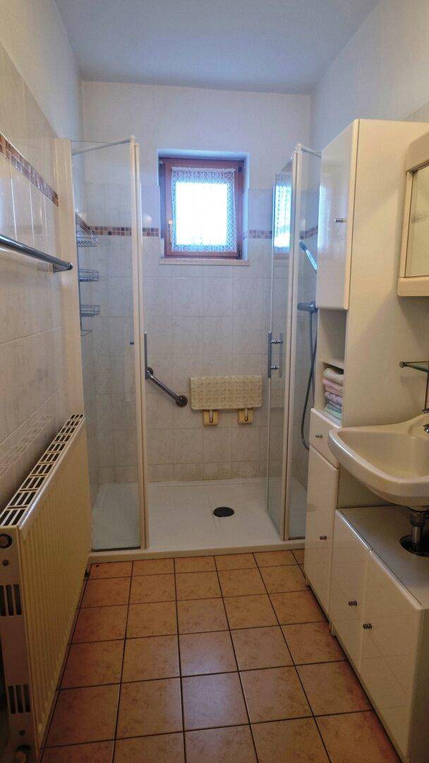 Badezimmer mit Duschkabine, Fliesenboden und einem Fenster für Tageslicht.