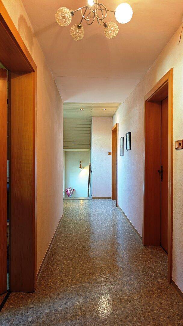 Langer Flur mit Terrazzoboden und Holztüren, der zu weiteren Räumen führt.