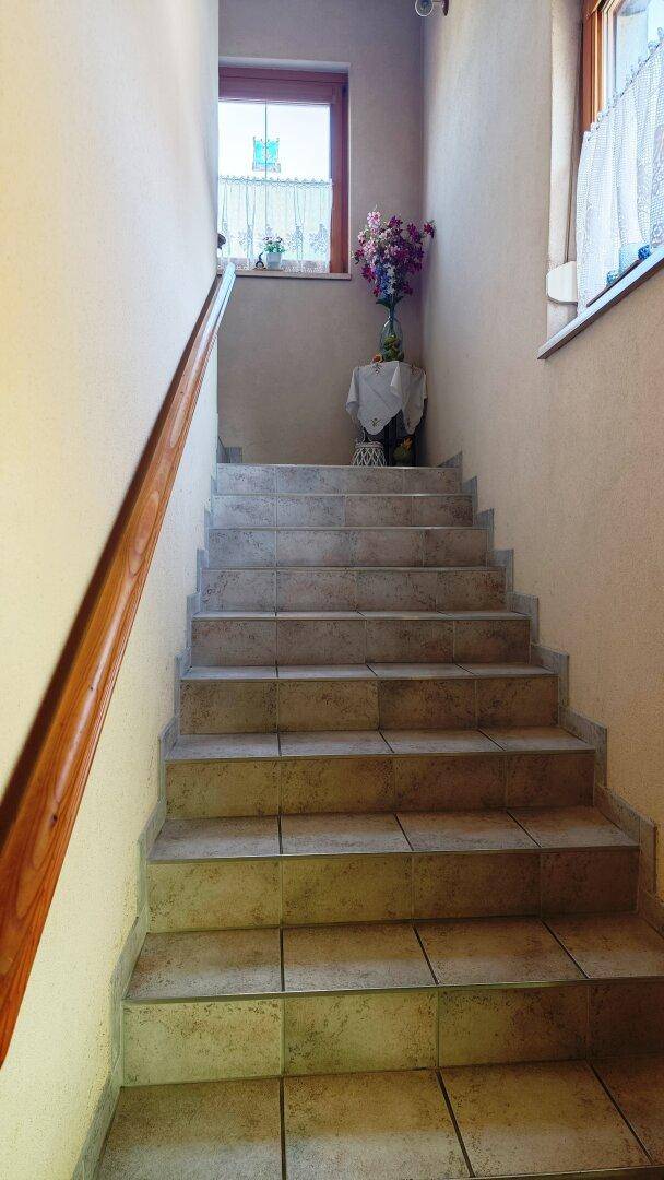 Geflieste Treppe mit Holzgeländer führt zu einem oberen Stockwerk mit Fenster.