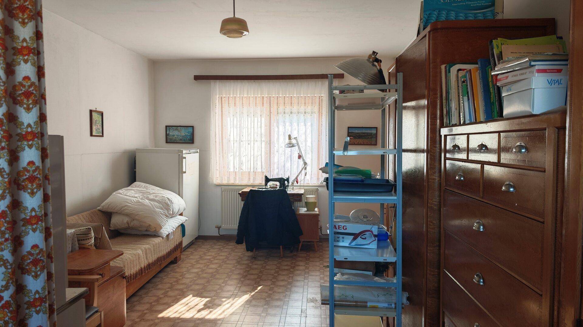 Heller Raum mit Schlafsofa, Schreibtisch am Fenster und praktischen Regalen.
