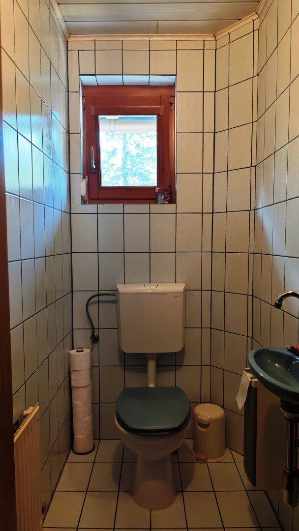 Separate Toilette mit Fenster, Waschbecken und Fliesenboden, einfach ausgestattet.
