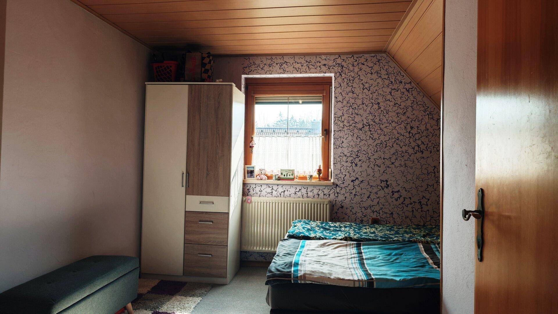 Schlafzimmer im Dachgeschoss mit Schräge, Kleiderschrank und Fenster.