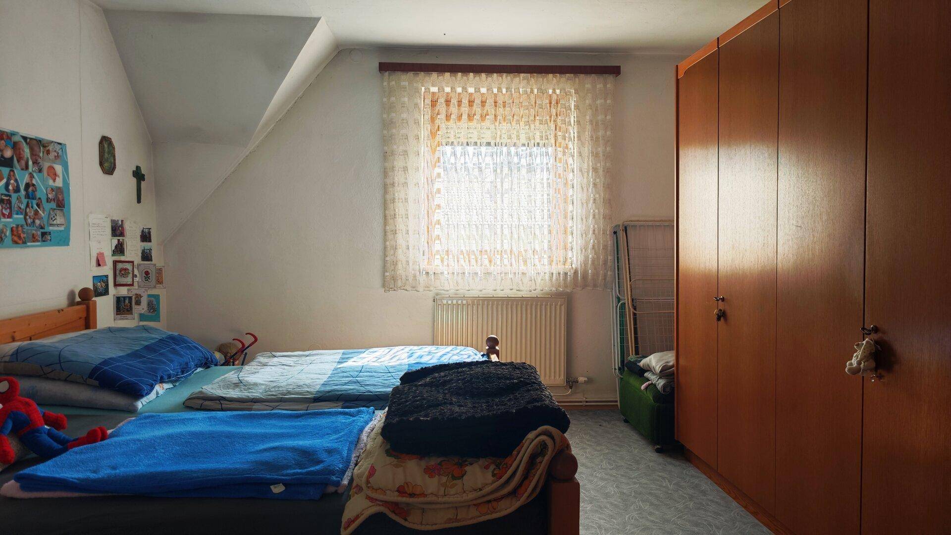 Helles Schlafzimmer im Dachgeschoss mit zwei Betten und großem Fenster.