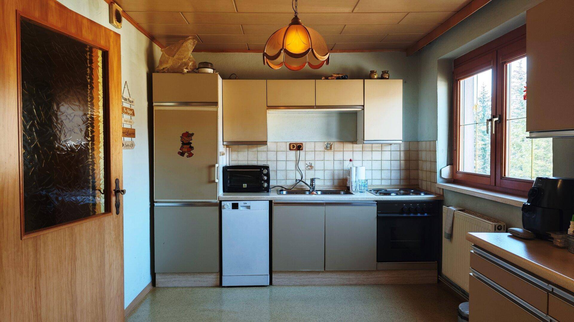 Funktionale Küche mit beigen Schränken, integrierten Geräten und Fensterblick.