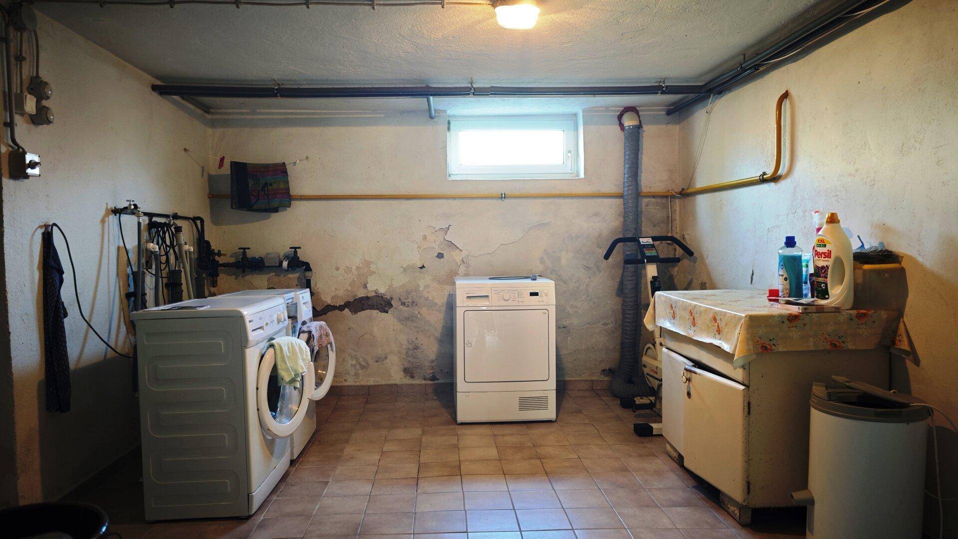 Waschküche im Keller mit Waschmaschine, Trockner und kleinem Fenster.