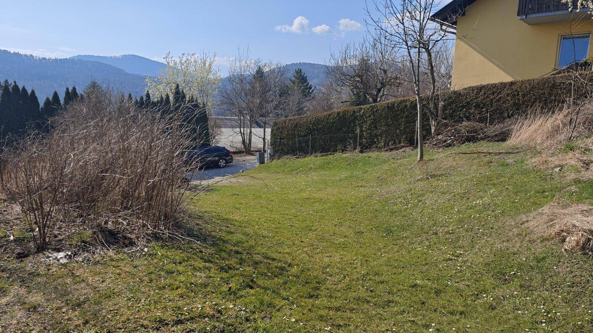 Grünfläche neben einem Haus mit Blick auf einen See und die dahinterliegenden Berge.