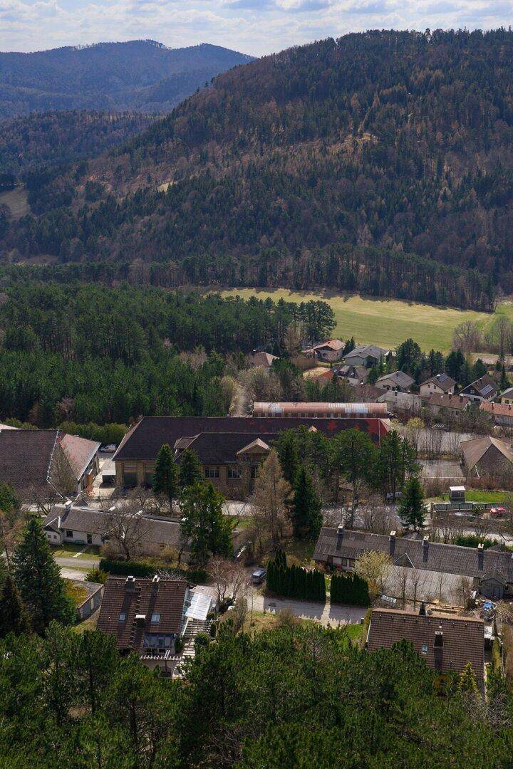 Hohe Luftaufnahme eines Tals mit Häusern, Feldern und dichten Wäldern, umgeben von Bergen.