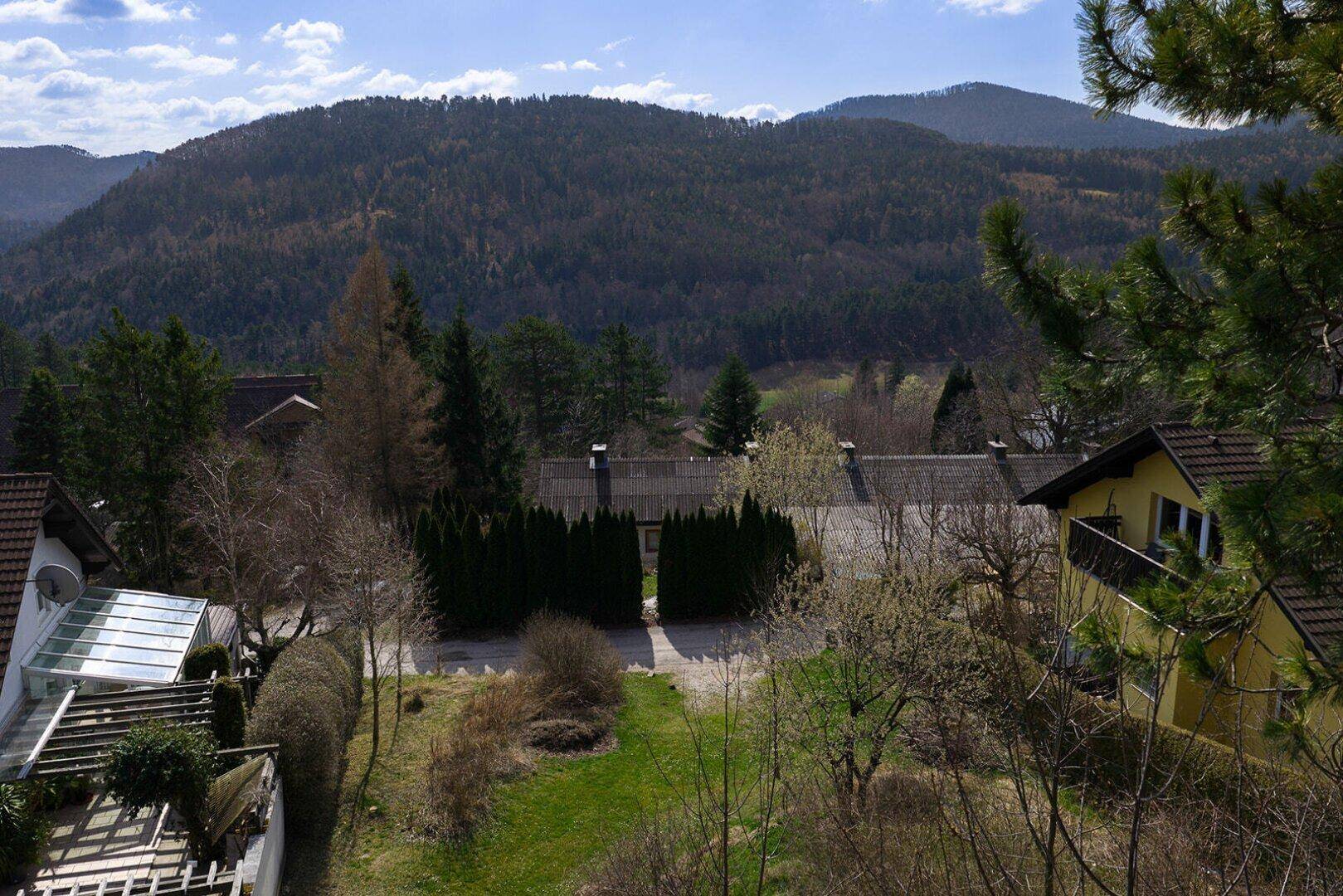 Panoramablick von erhöhter Position auf Wohnhäuser, Wälder und die umliegende Berglandschaft.