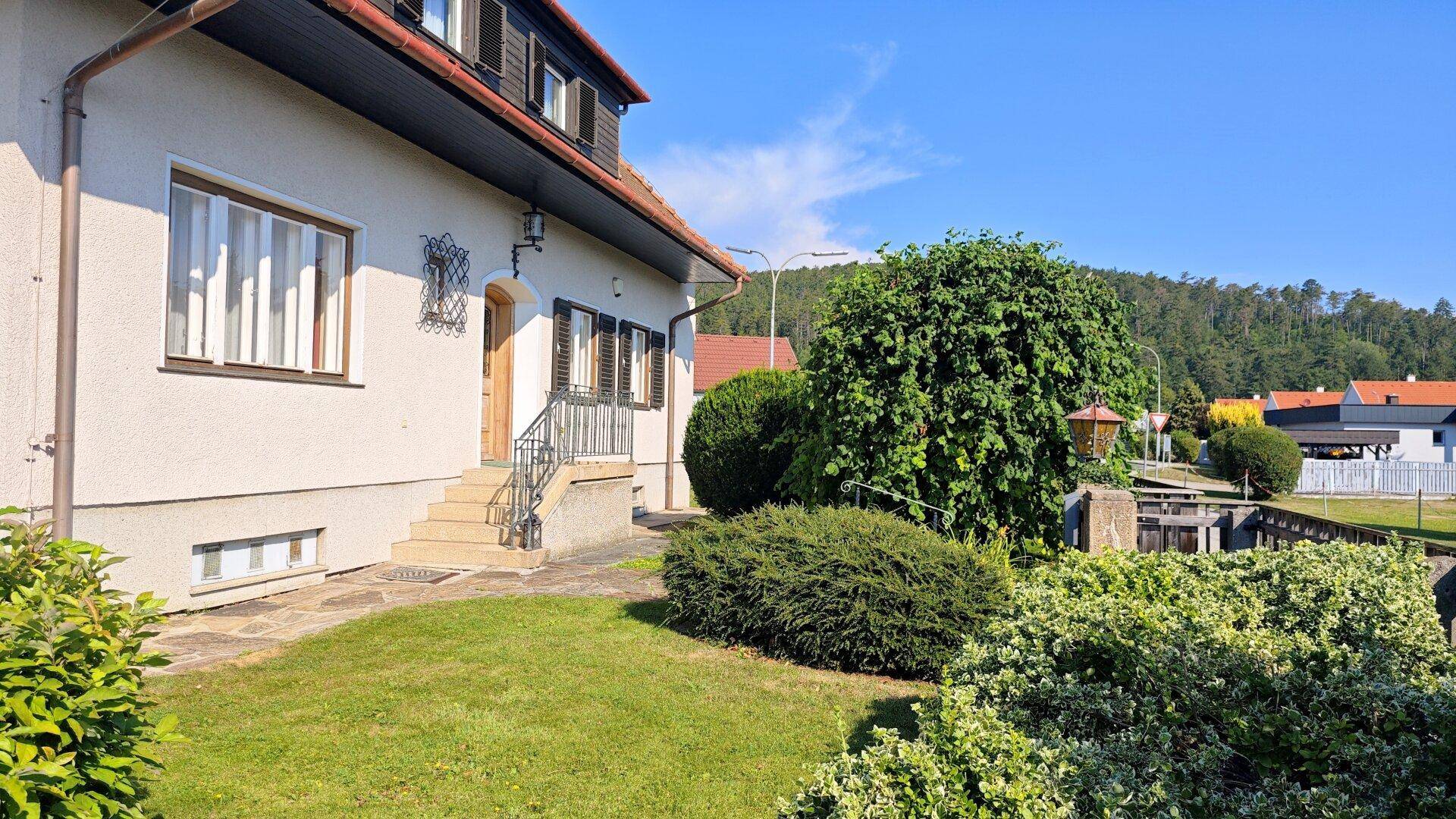Eingangsbereich des Hauses mit Treppe und einem gepflegten Vorgarten mit üppigem Grün.