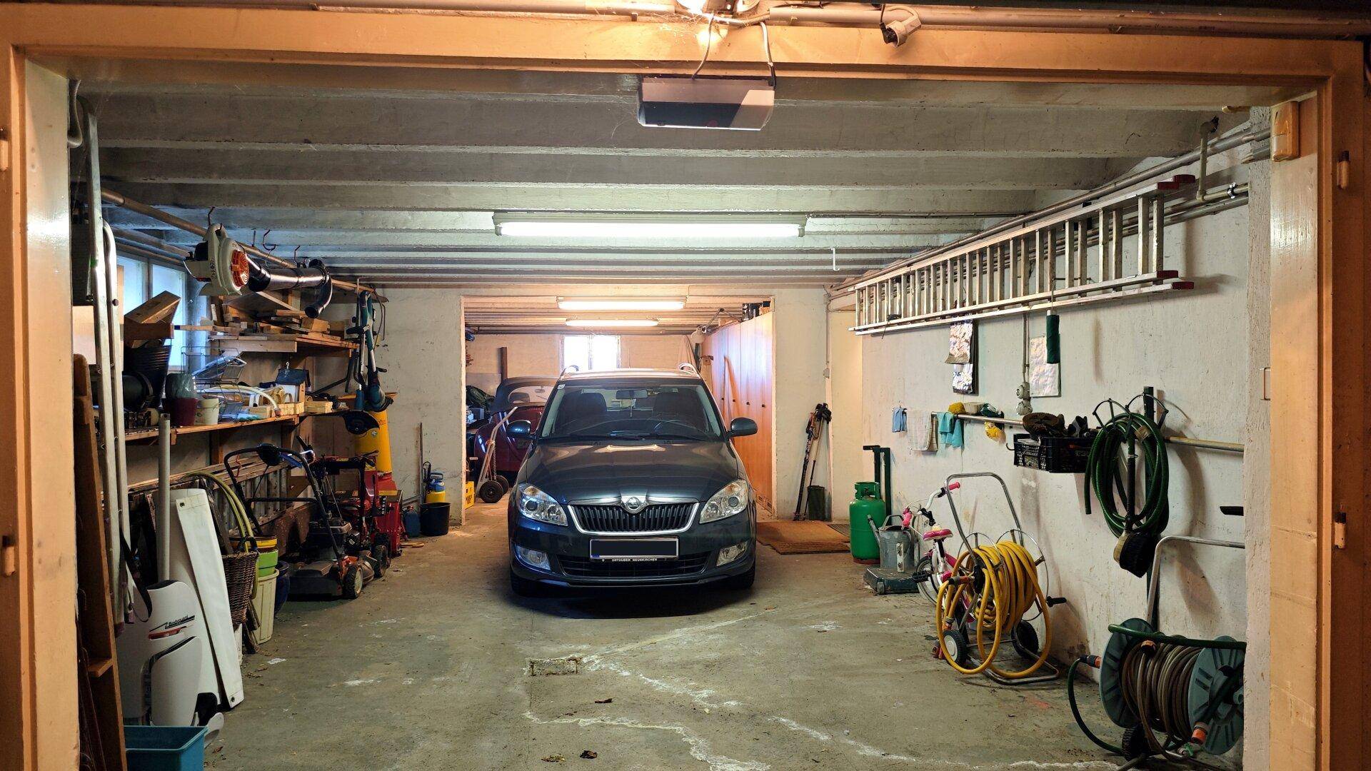 Geräumige Garage mit einem geparkten Auto, Werkzeugen und Lagerregalen an den Wänden.