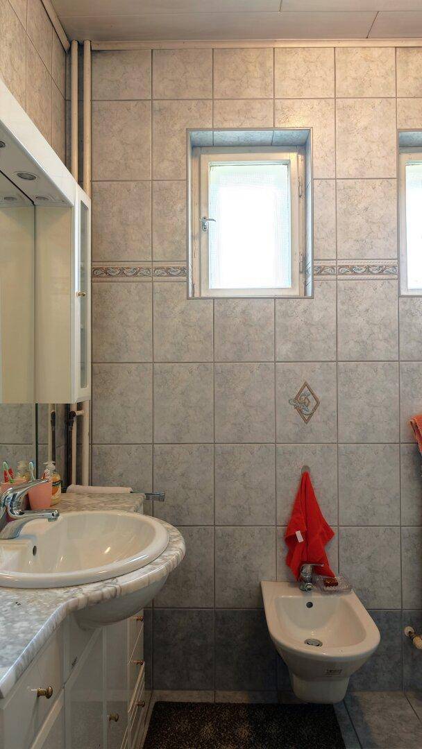 Badezimmer mit Fliesen, Einzelwaschbecken, Bidet und Fenster, das für natürliche Belüftung sorgt.