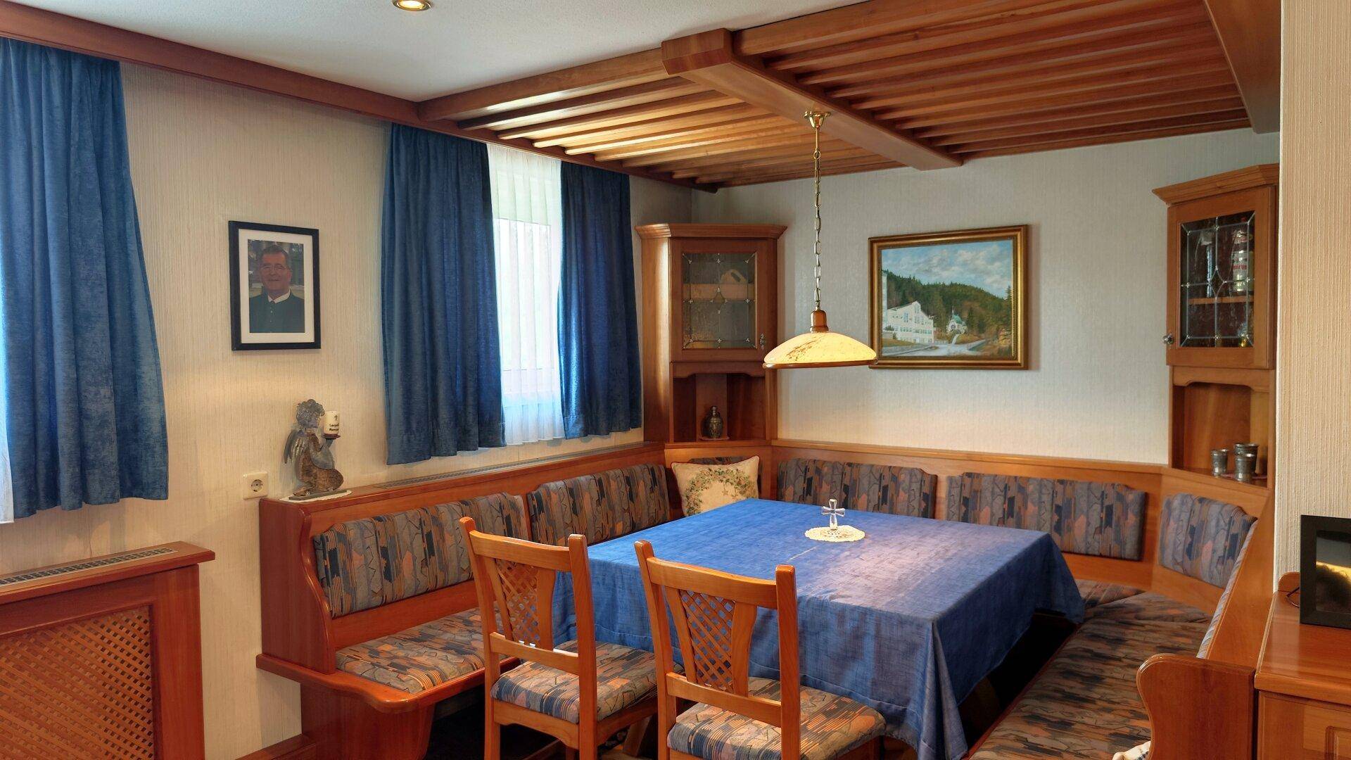 Traditioneller Essbereich mit Eckbank, Holzbalkendecke und blauen Vorhängen, gemütlich eingerichtet.