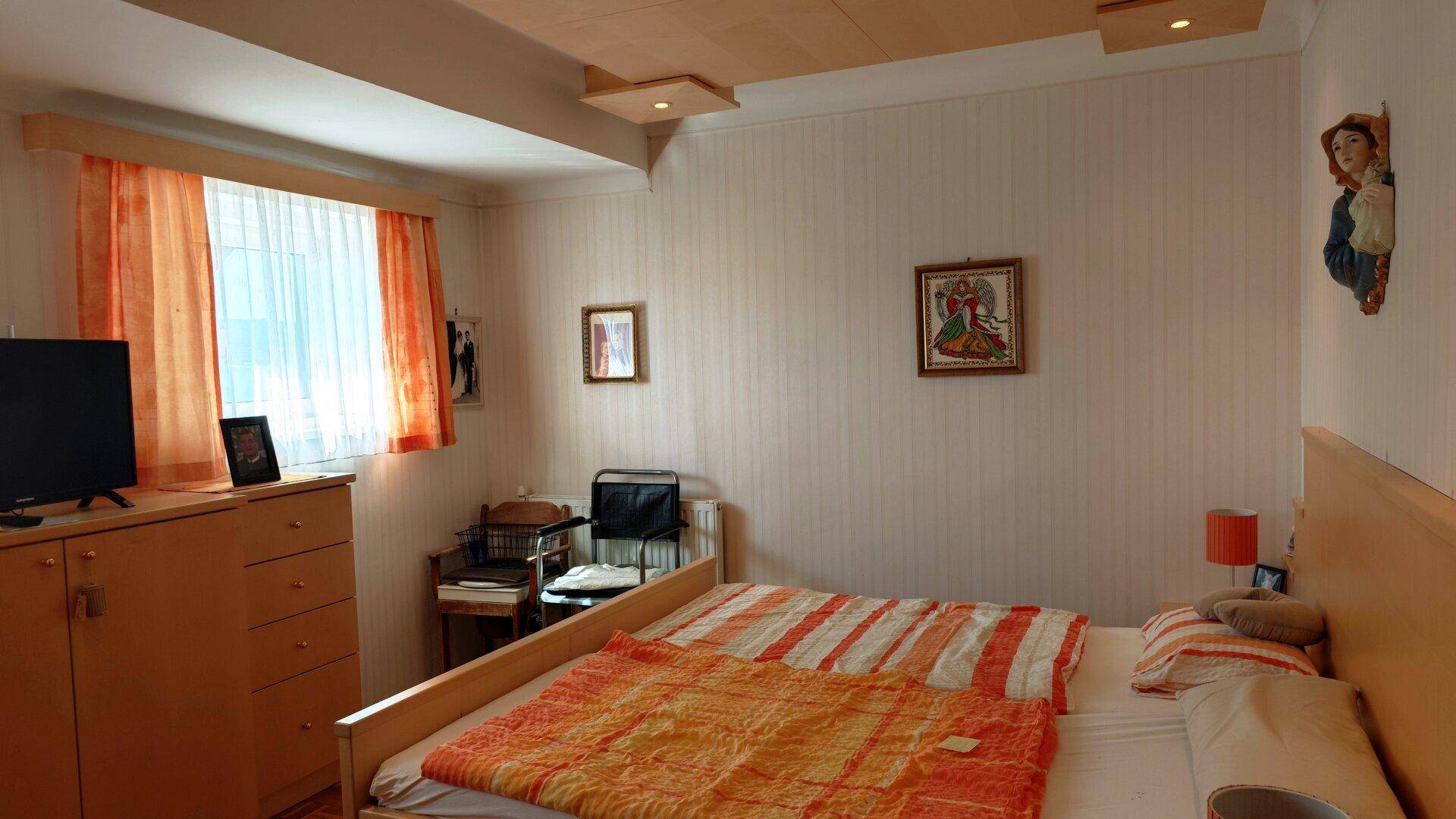 Gemütliches Schlafzimmer mit Doppelbett, Holzdecke und Fenster mit orangefarbenen Vorhängen.