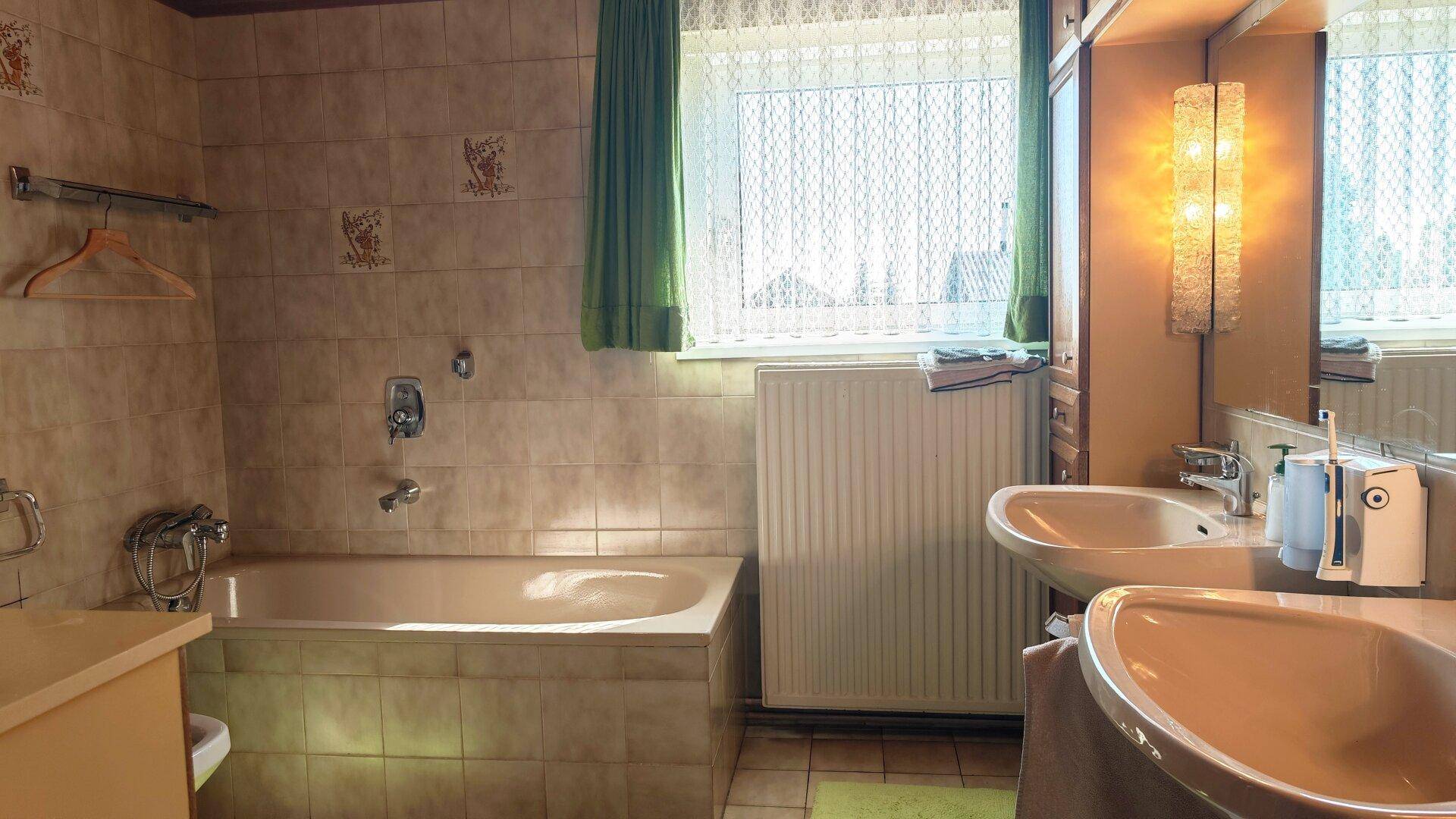 Helles Badezimmer mit Badewanne, Doppelwaschbecken und Fenster für natürliches Tageslicht.