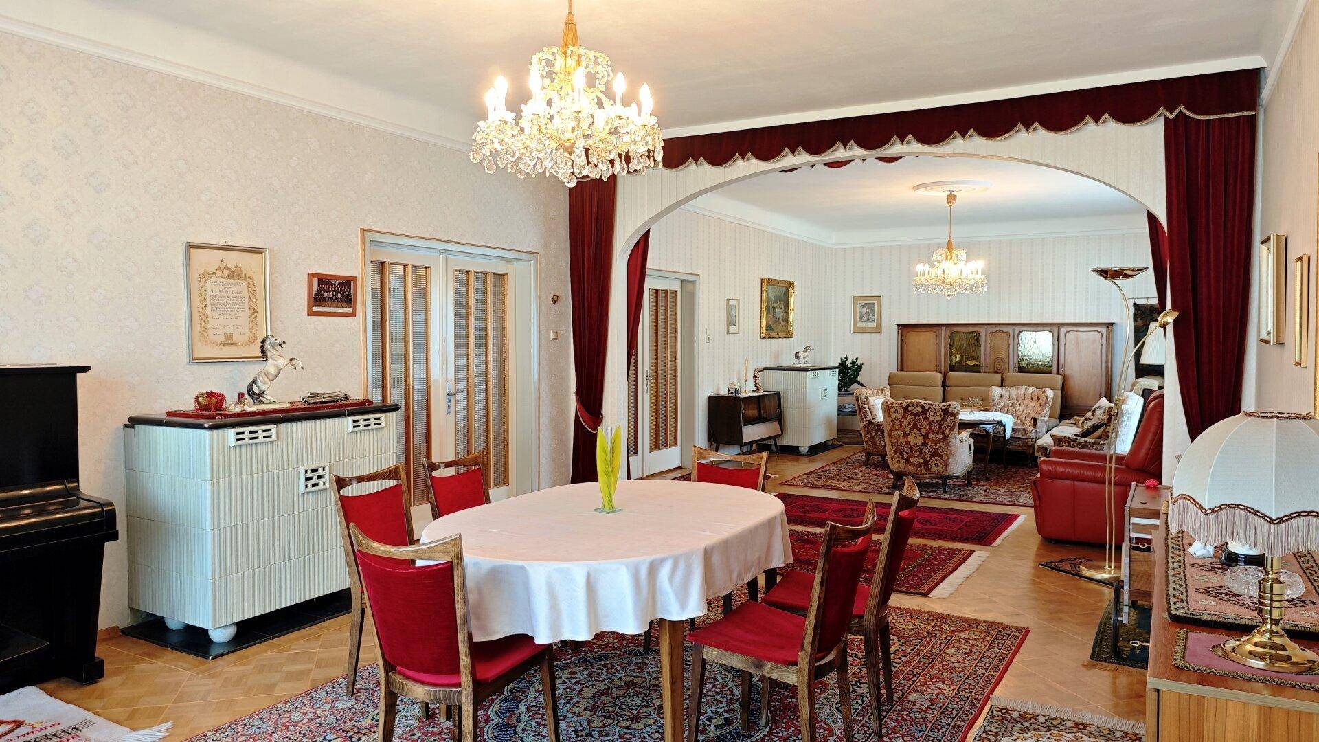 Eleganter Wohn-Essbereich mit Kronleuchtern, Parkettboden und traditionellen Möbeln, durch einen Bogen verbunden.