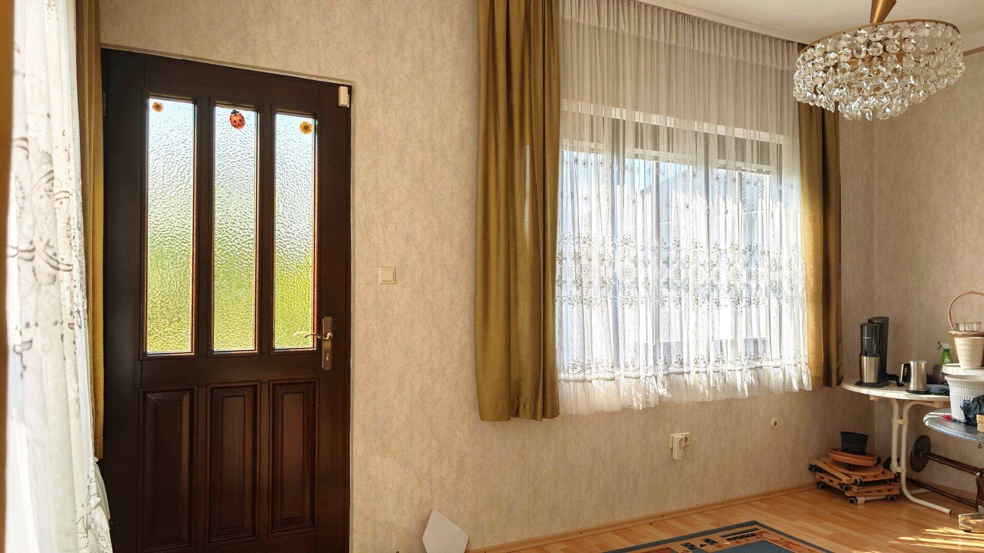 Heller Raum mit Holztür, großem Fenster und Kronleuchter, der viel Tageslicht empfängt.