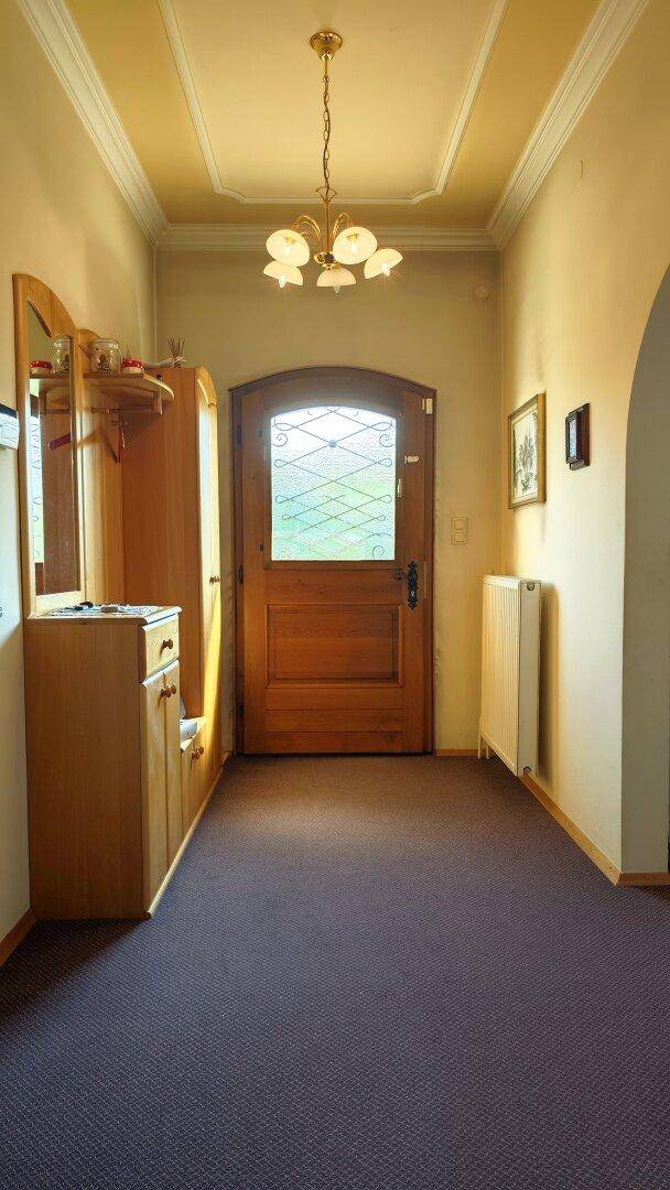 Heller Eingangsbereich mit Holztür, Garderobe und Teppichboden, der zum Inneren des Hauses führt.