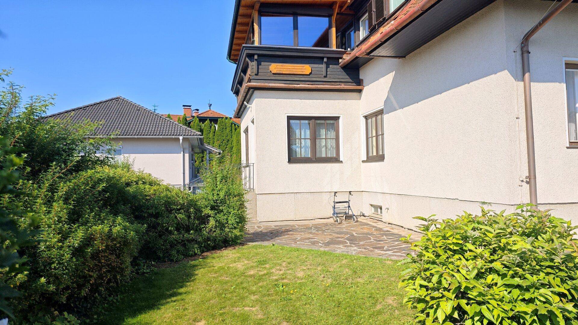 Seitlicher Gartenbereich mit kleiner gepflasterter Terrasse und gepflegtem Rasen neben dem Haus.
