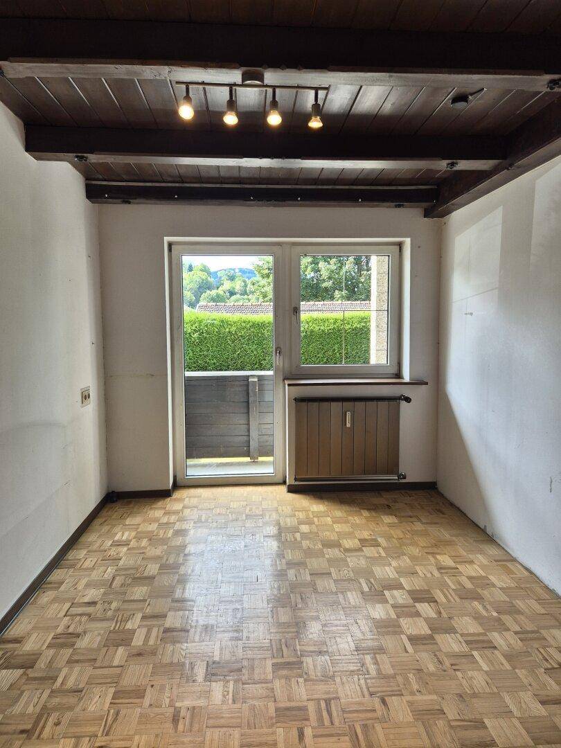 Heller Raum mit Parkettboden, Holzbalkendecke und Fenster mit Blick ins Grüne.