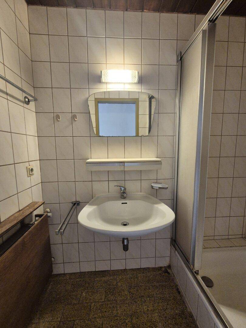 Badezimmer mit Fliesen, Waschbecken, Spiegel und Duschkabine, in gutem Zustand.