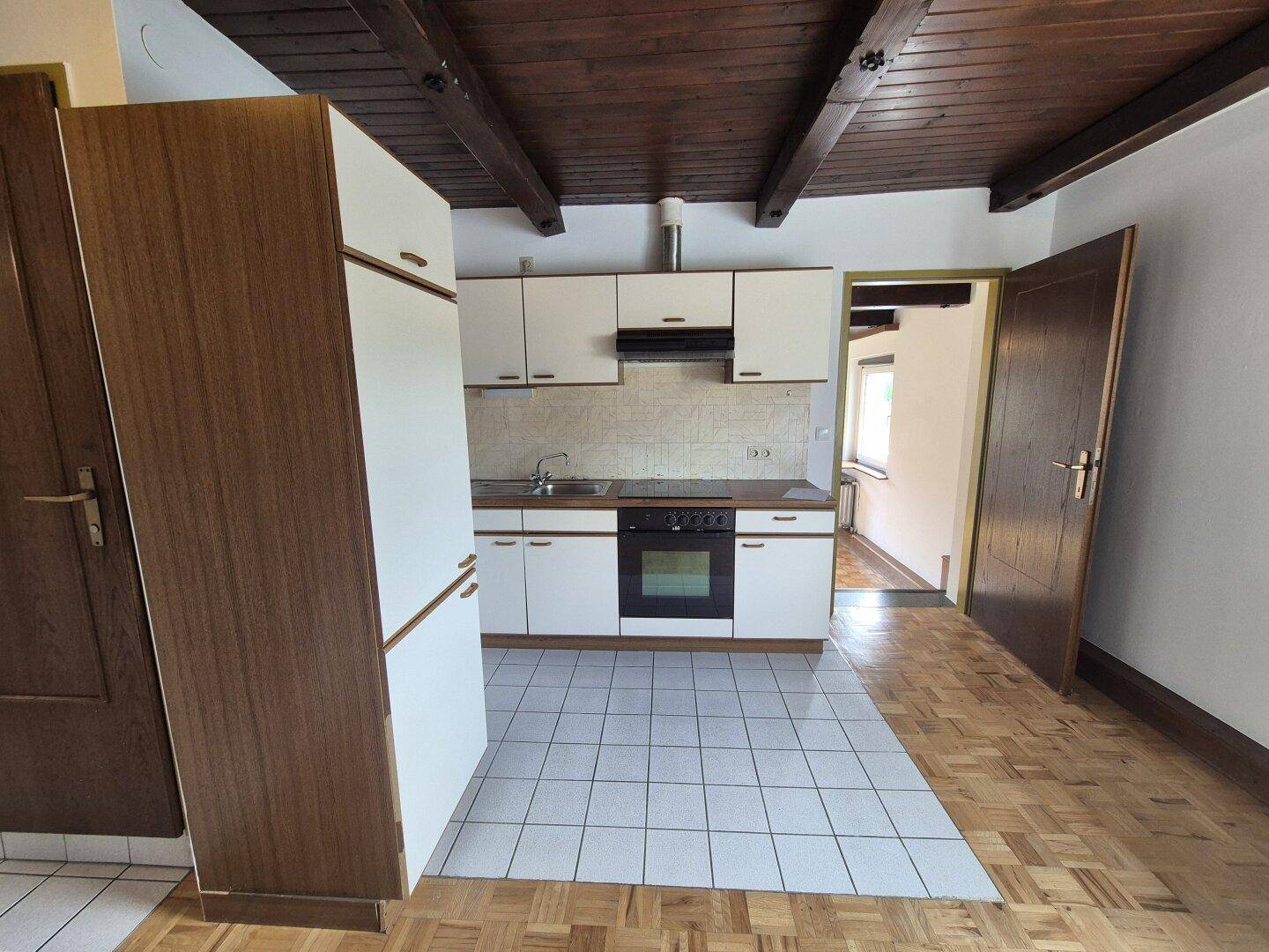 Küche mit weißen Einbauschränken, Herd und Kühlschrank, kombiniert mit Fliesen- und Parkettboden.