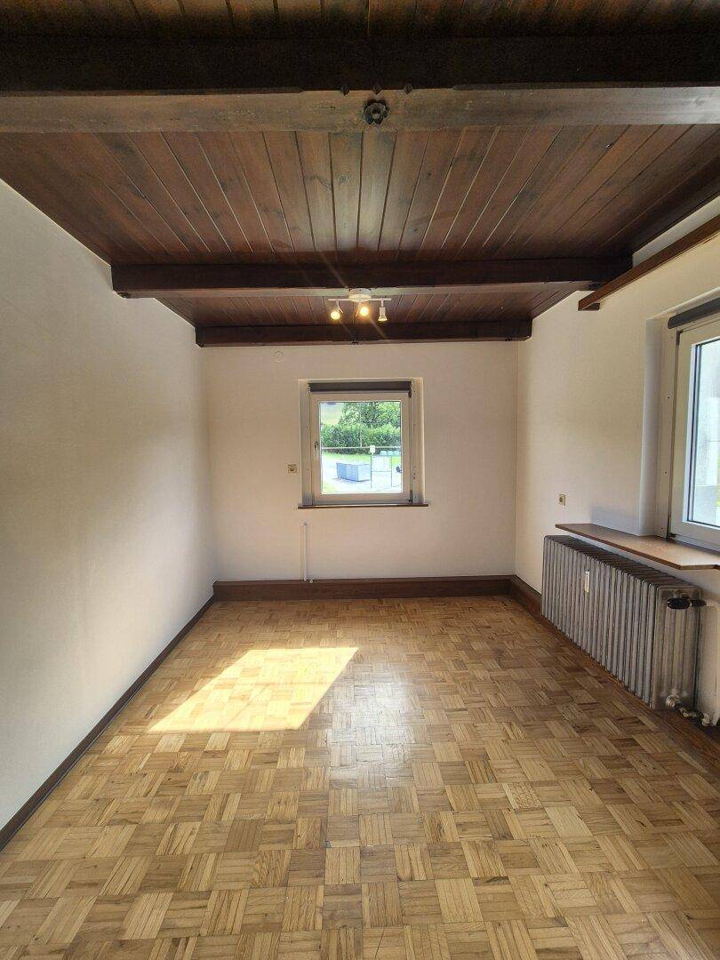 Heller Raum mit Parkettboden, dunkler Holzdecke und einem Fenster, das viel Tageslicht hereinlässt.