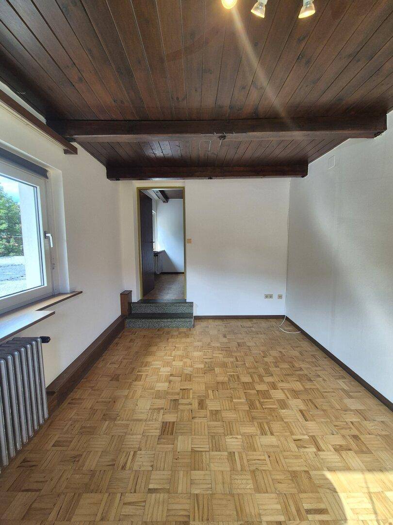 Geräumiger Wohnraum mit Parkettboden, Holzbalkendecke und Zugang zu einem gefliesten Flur.
