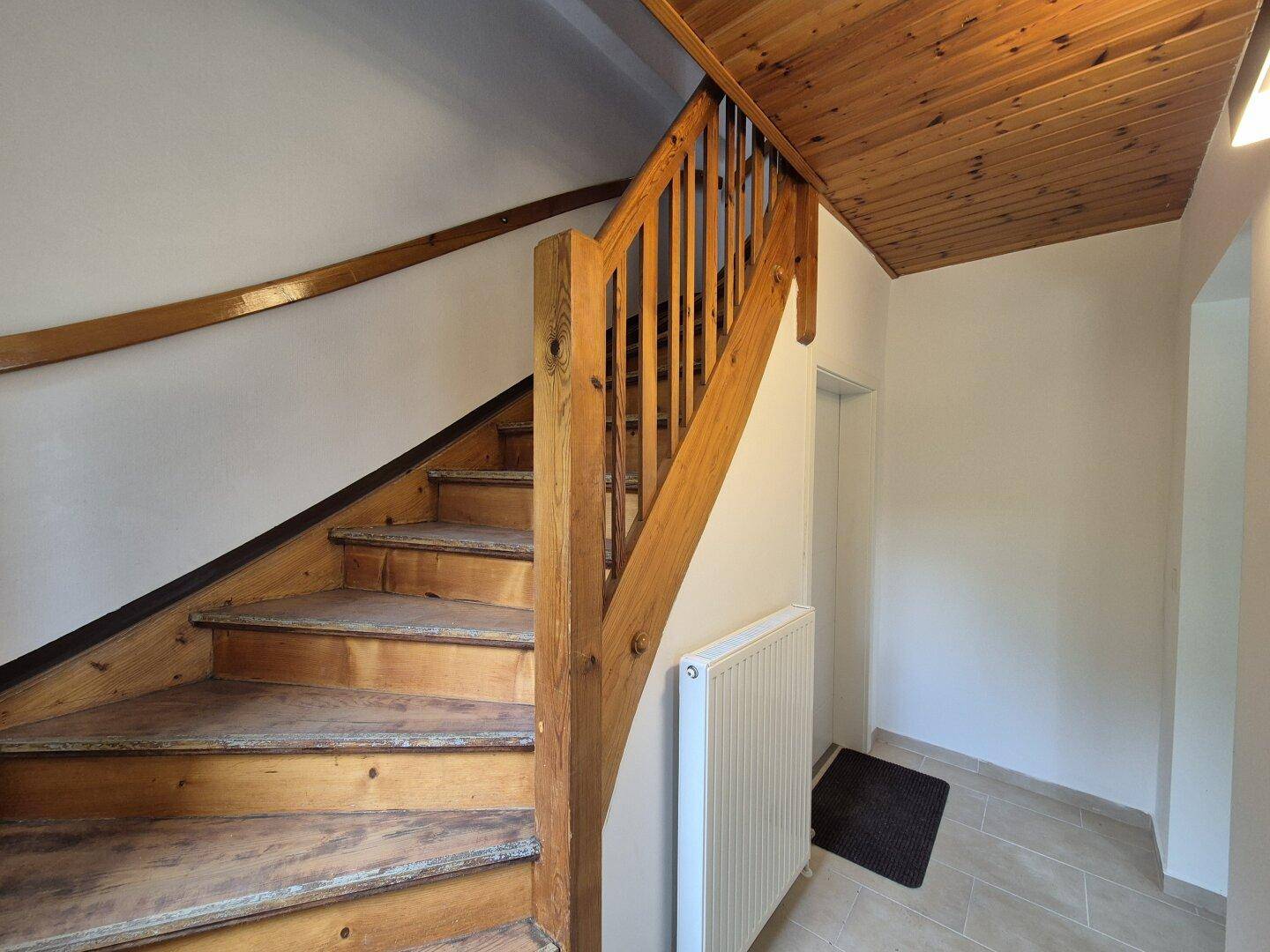 Holztreppe mit Geländer und Holzdecke, die in die obere Etage führt.