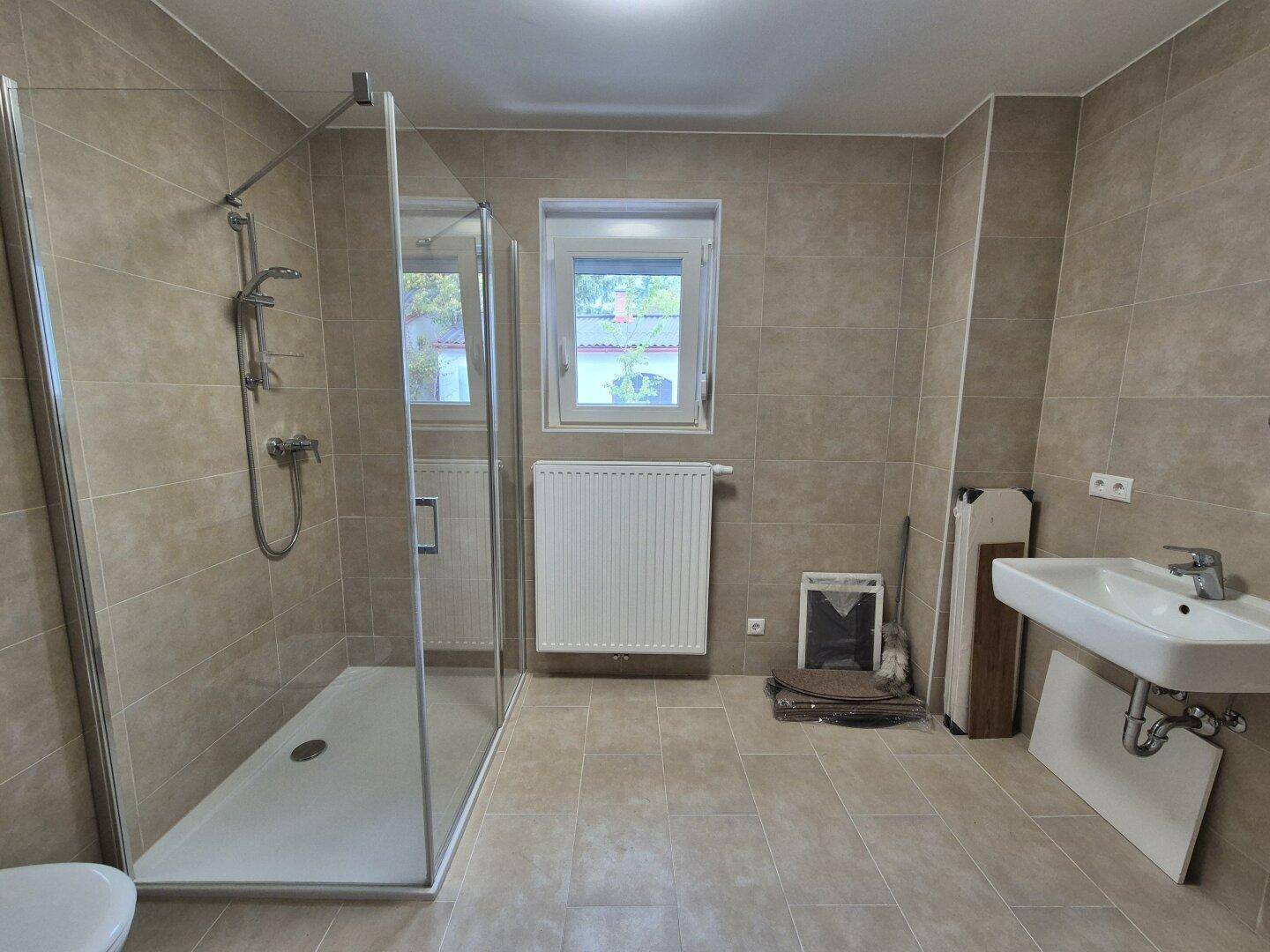 Modernes Badezimmer mit beigefarbenen Fliesen, Duschkabine und Fenster.