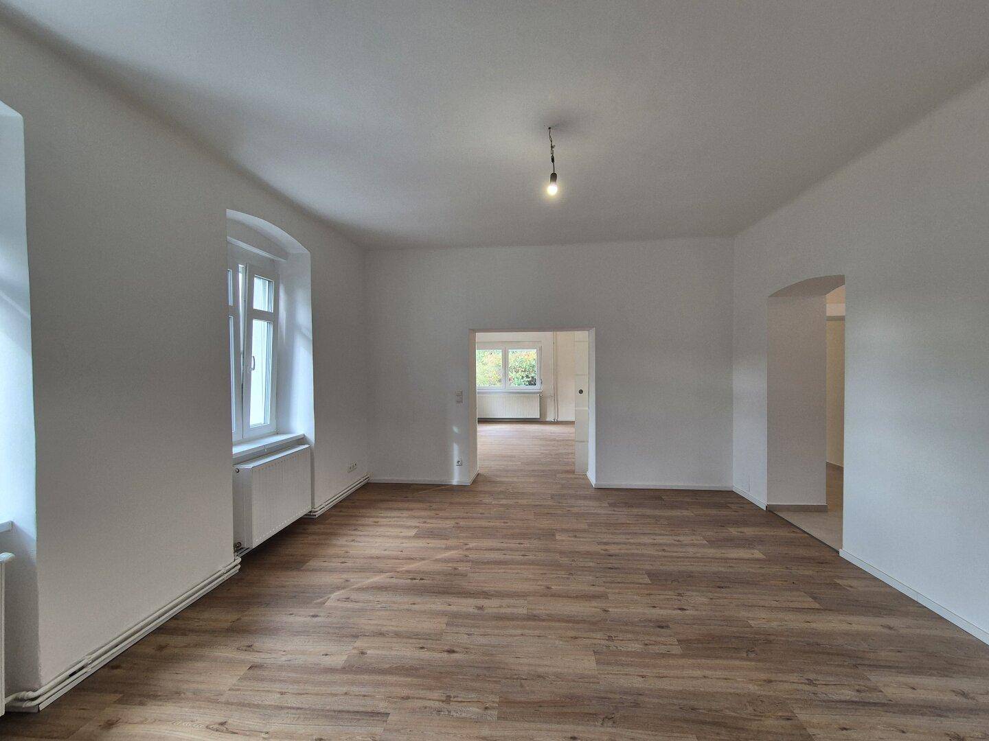 Geräumiges Wohnzimmer mit neuem Laminatboden und Zugang zu weiteren Räumen.
