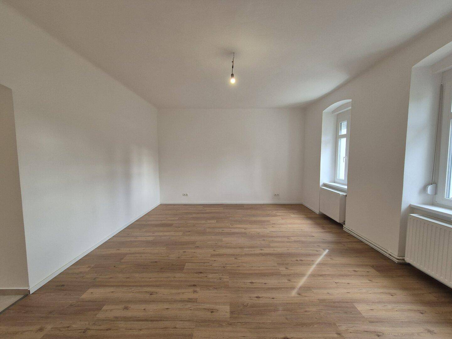 Helles Wohnzimmer mit Laminatboden und mehreren Fenstern, bereit zur Einrichtung.