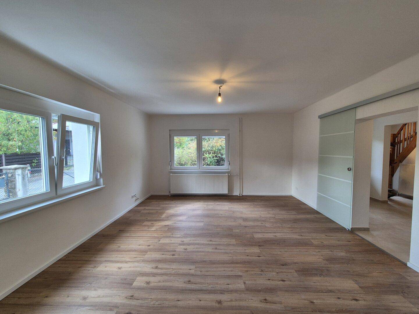 Wohnzimmer mit Laminatboden, großen Fenstern und einer modernen Glasschiebetür.