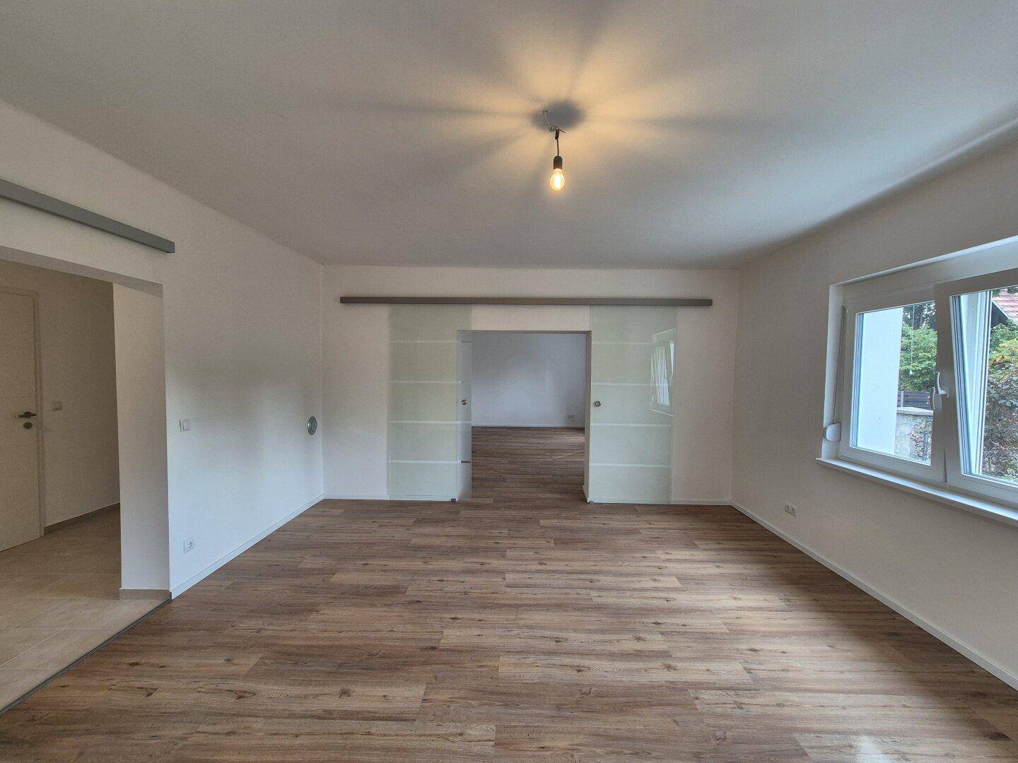 Heller Wohnbereich mit Laminatboden und einer eleganten Glasschiebetür zu einem weiteren Raum.