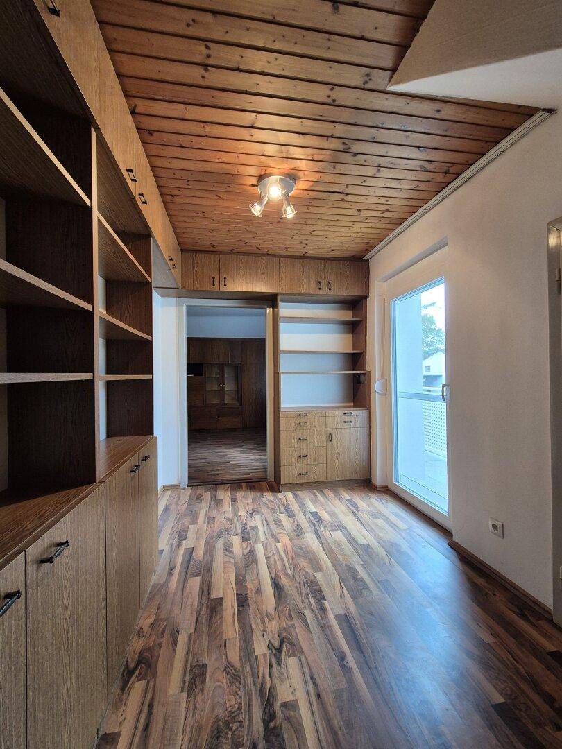Raum mit Holzboden, Holzdecke und eingebauten Holzregalen, ideal als Büro oder Bibliothek.