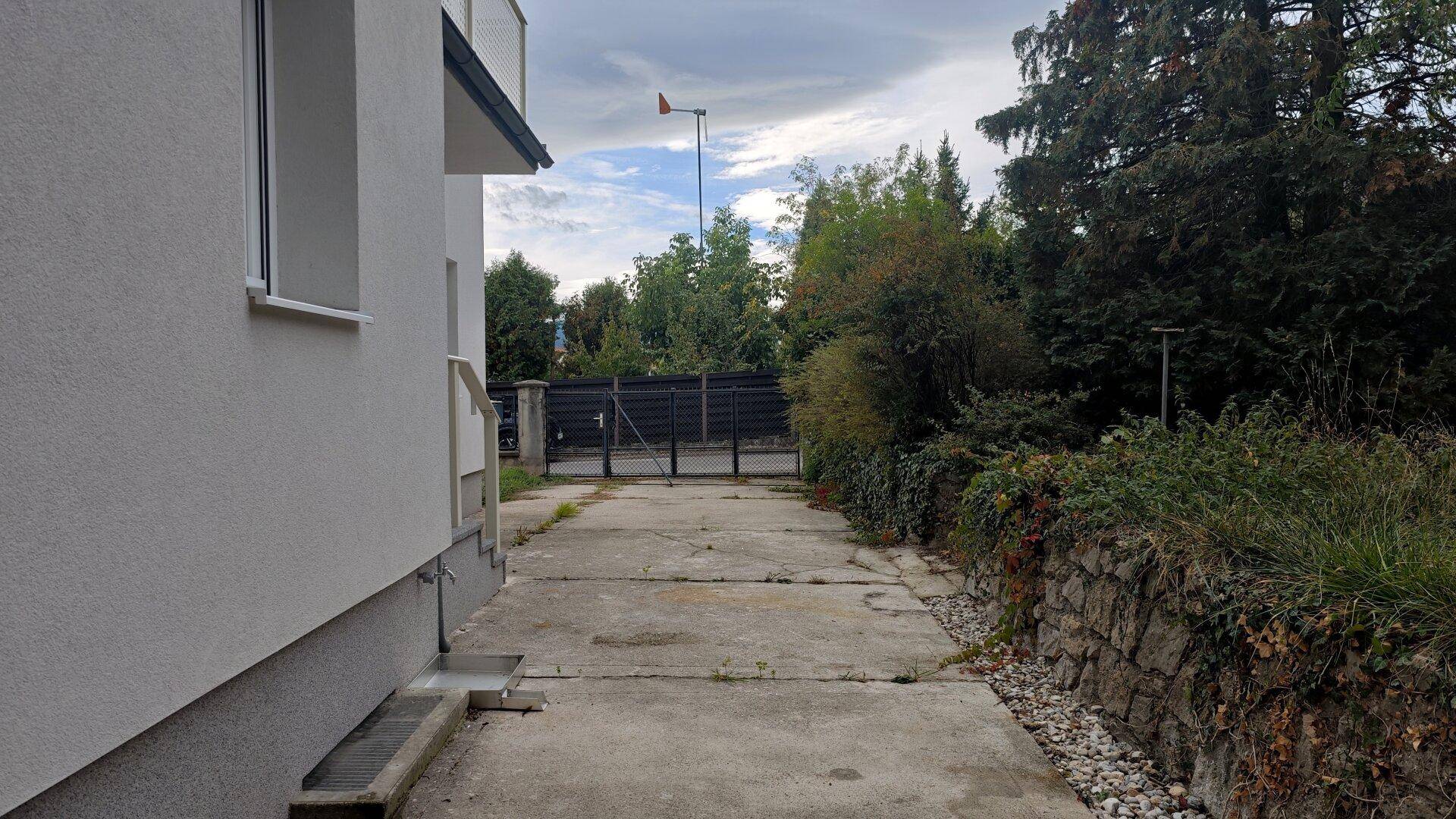 Seitenansicht des Hauses mit Zufahrt und einer Steinmauer im Gartenbereich.