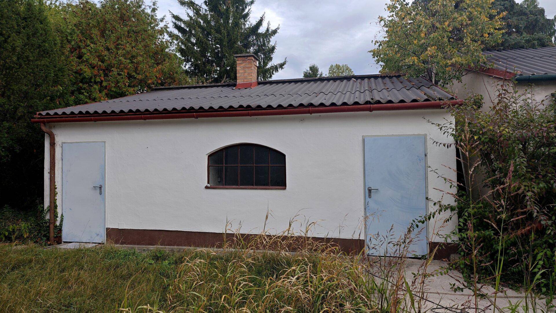 Kleines Nebengebäude mit zwei Türen und einem Bogenfenster im Gartenbereich.