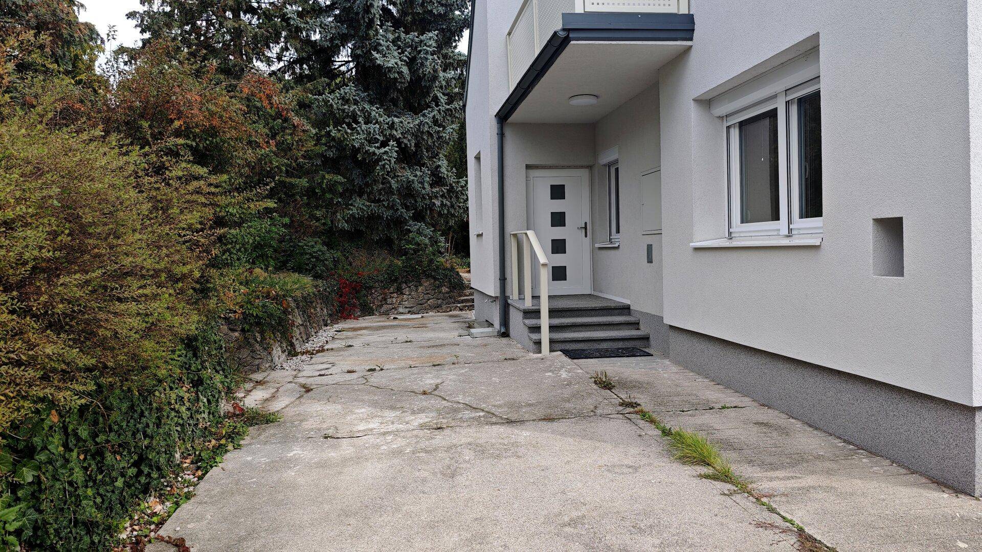Eingangsbereich des Hauses mit Treppe, Balkon und einer gepflasterten Zufahrt.