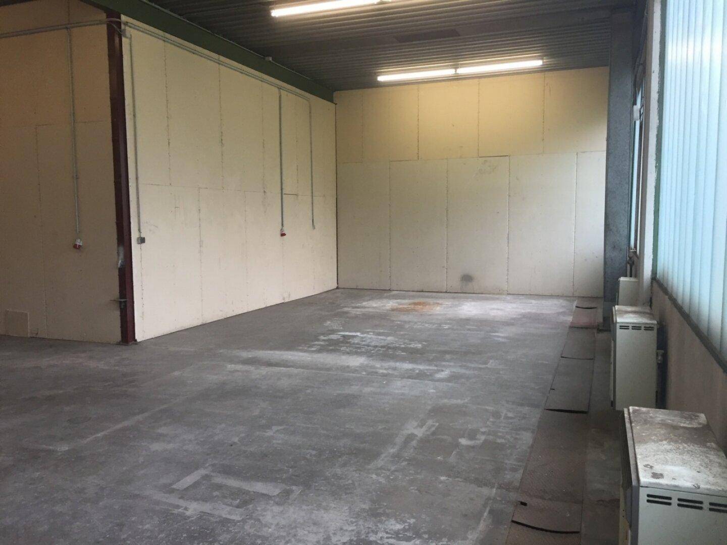Blick in eine saubere Lagerhalle mit Betonboden, hohen Decken und Wandheizkörpern.