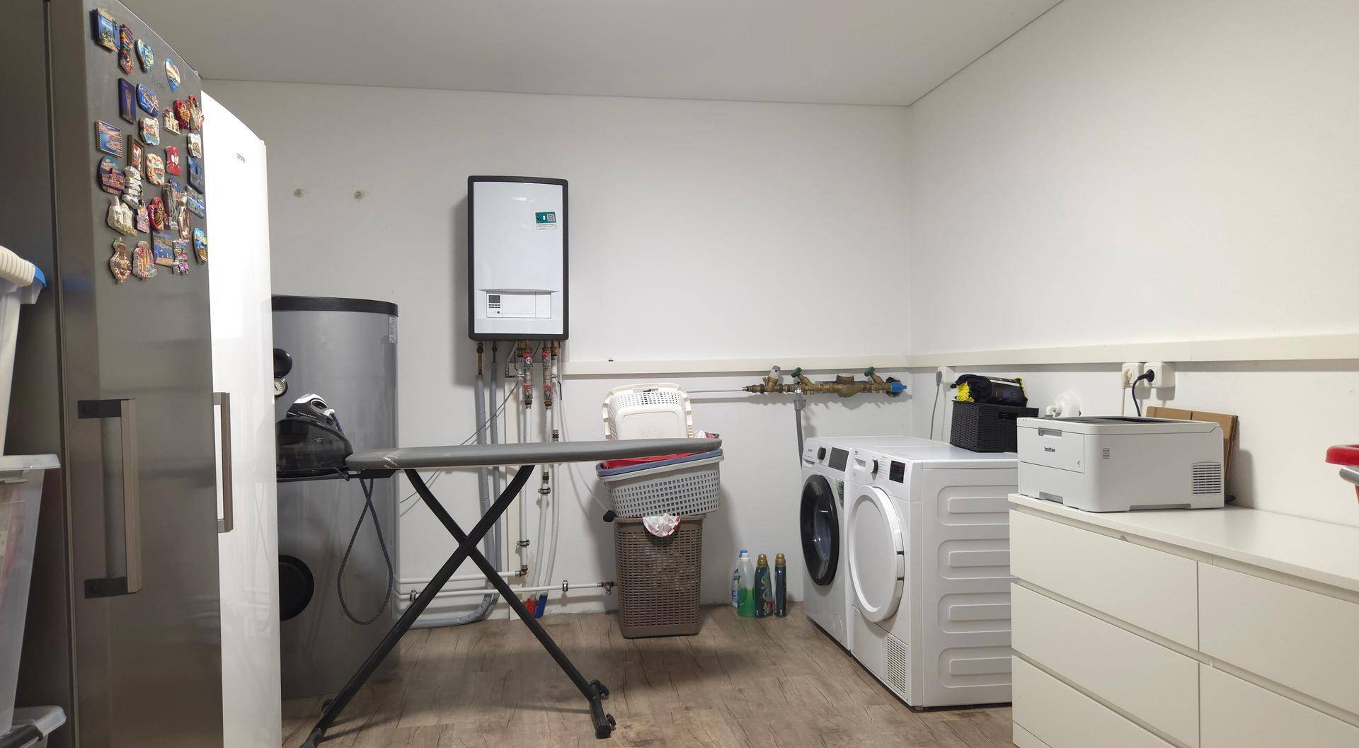 Praktischer Hauswirtschaftsraum mit Waschmaschine, Trockner, Bügelbrett und Heizungsanlage.