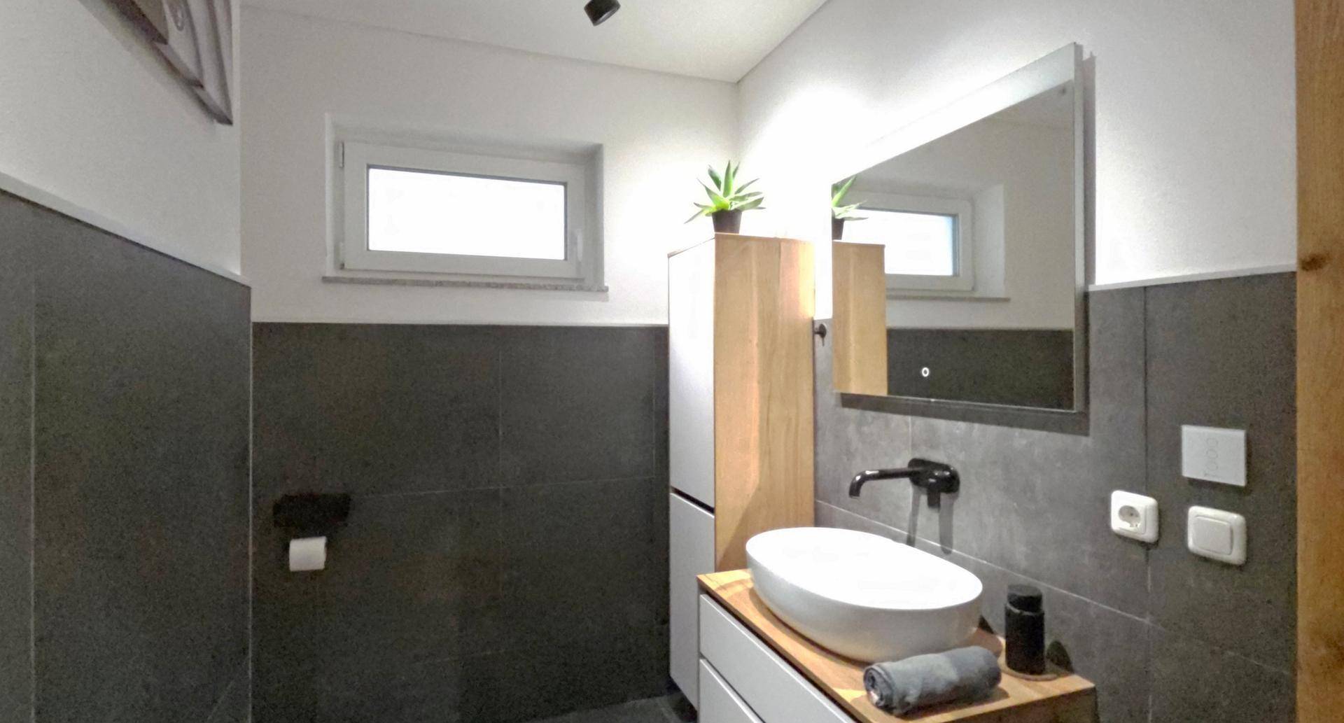 Modernes Badezimmer mit Aufsatzwaschbecken, Spiegelschrank und dunklen Wandfliesen.