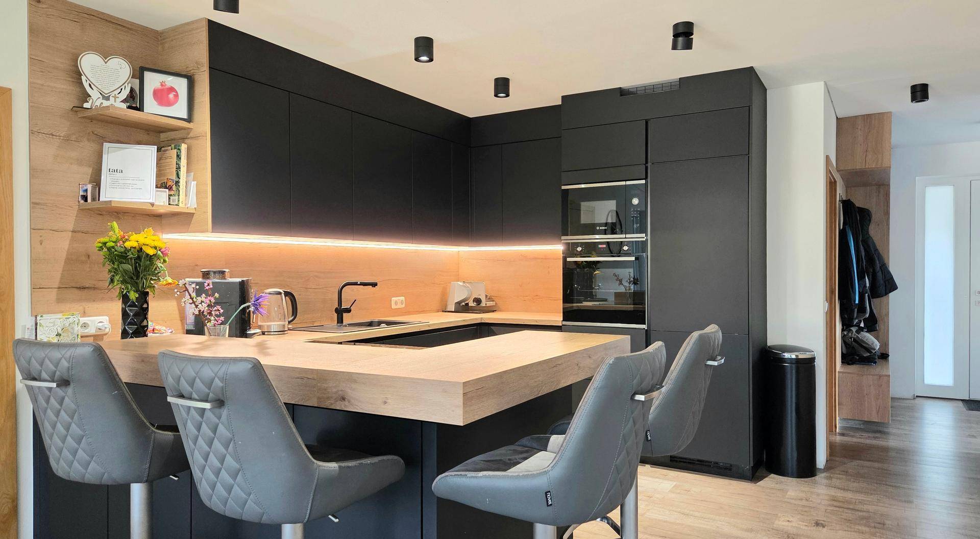 Moderne schwarze Küche mit Holz-Arbeitsplatte, integrierten Geräten und einer Frühstücksbar.