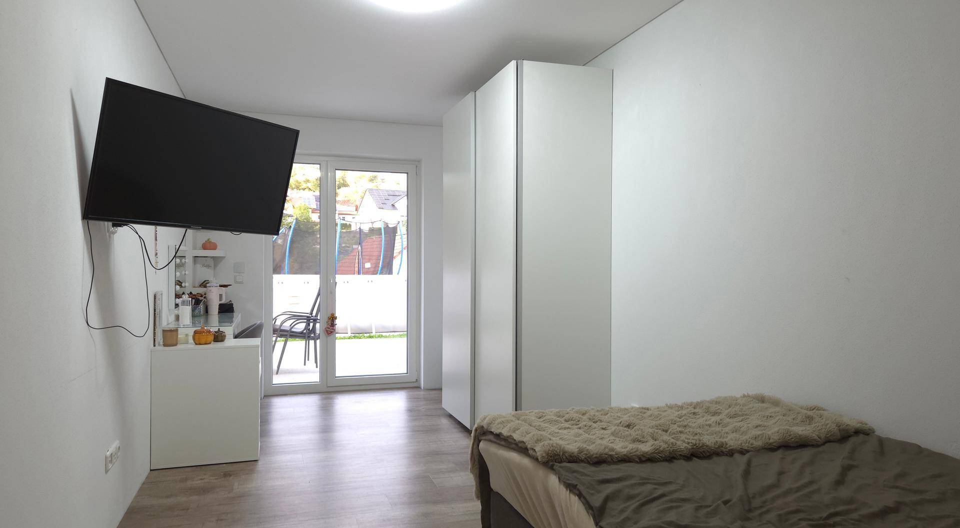Modern eingerichtetes Schlafzimmer mit Kleiderschrank, Fernseher und Zugang zum Garten.