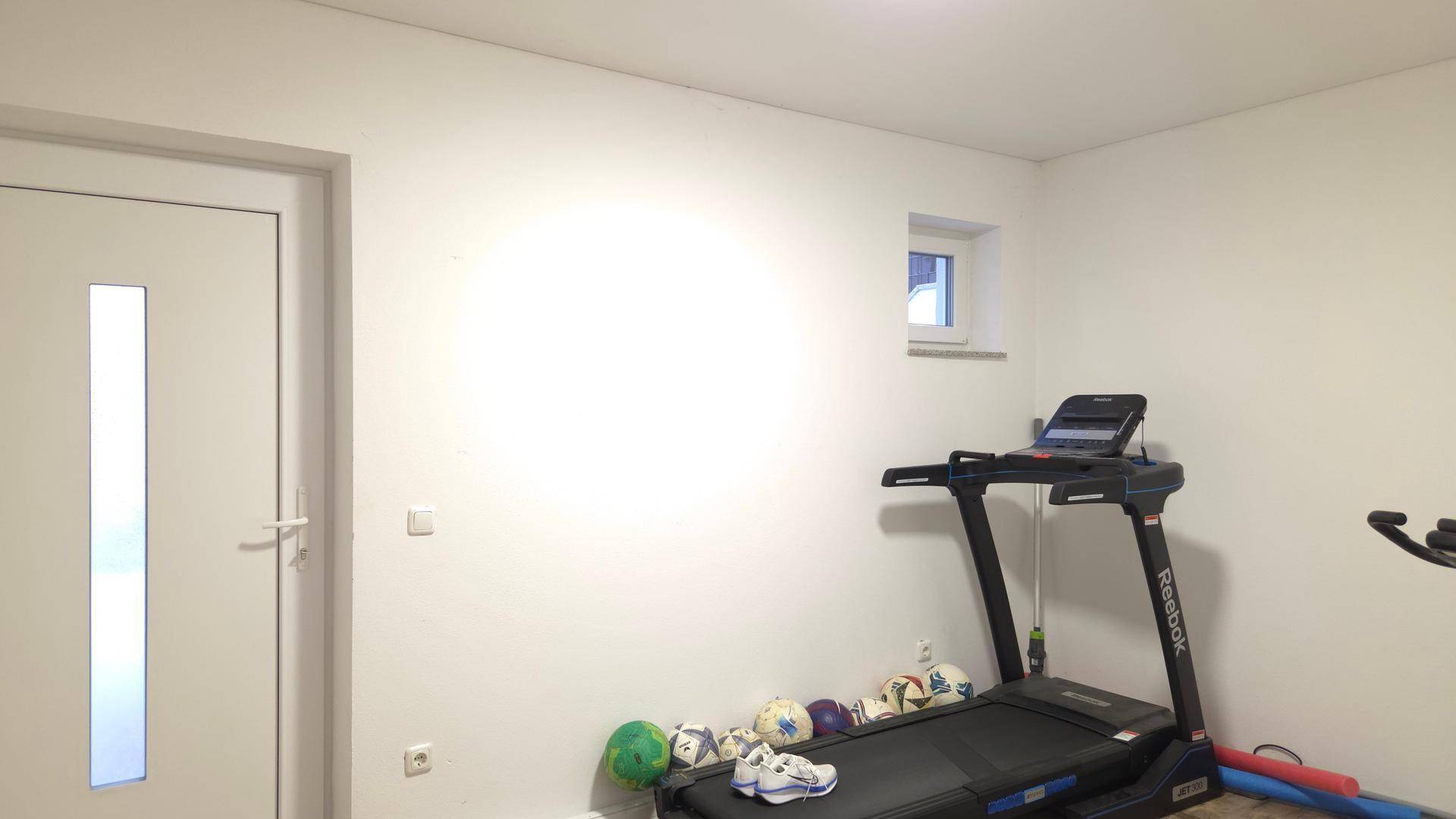 Kleiner Fitnessraum mit Laufband und Sportgeräten, ideal für das Training zu Hause.