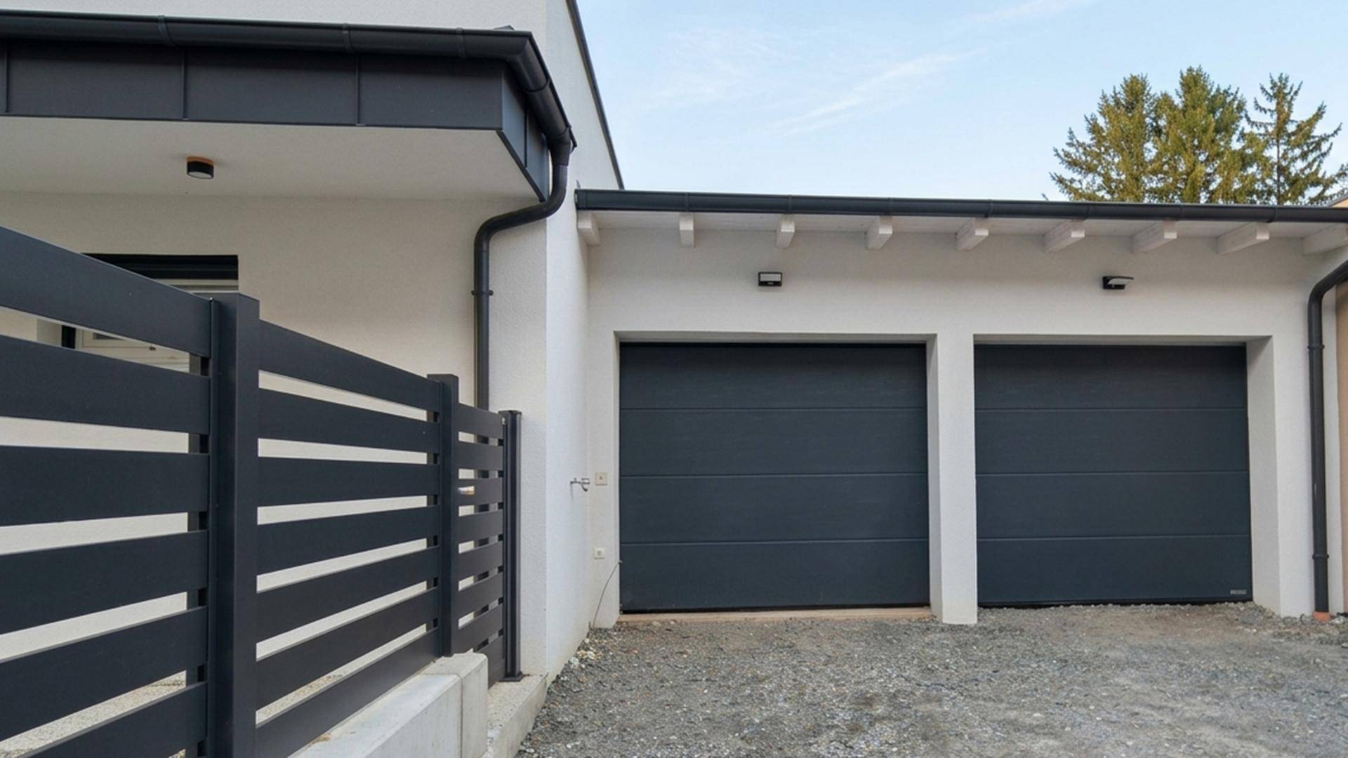 Doppelgarage mit modernen Toren und einem Zaun, der das Grundstück abgrenzt.