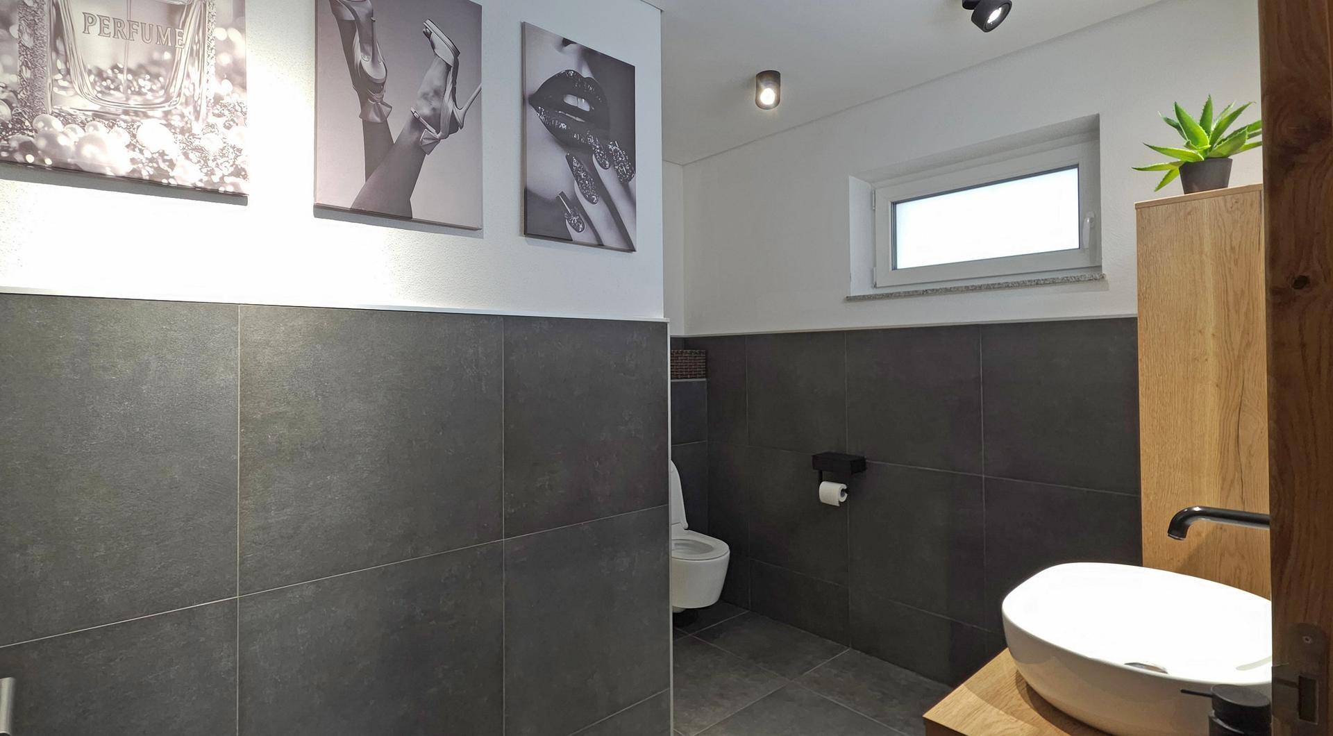 Modernes Gäste-WC mit dunklen Fliesen, Aufsatzwaschbecken und einem Fenster für Tageslicht.