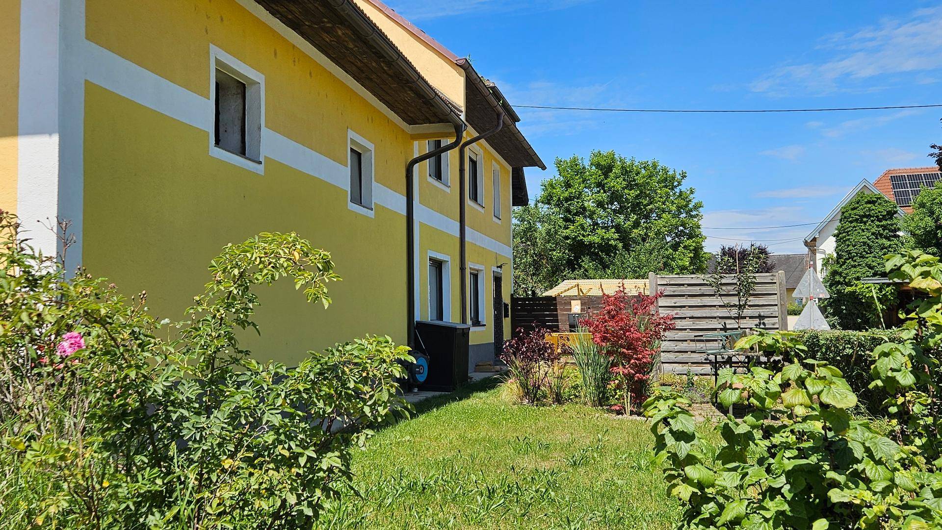 Gelbe Hausfassade mit Fenstern und einem gepflegten Gartenbereich im Vordergrund.