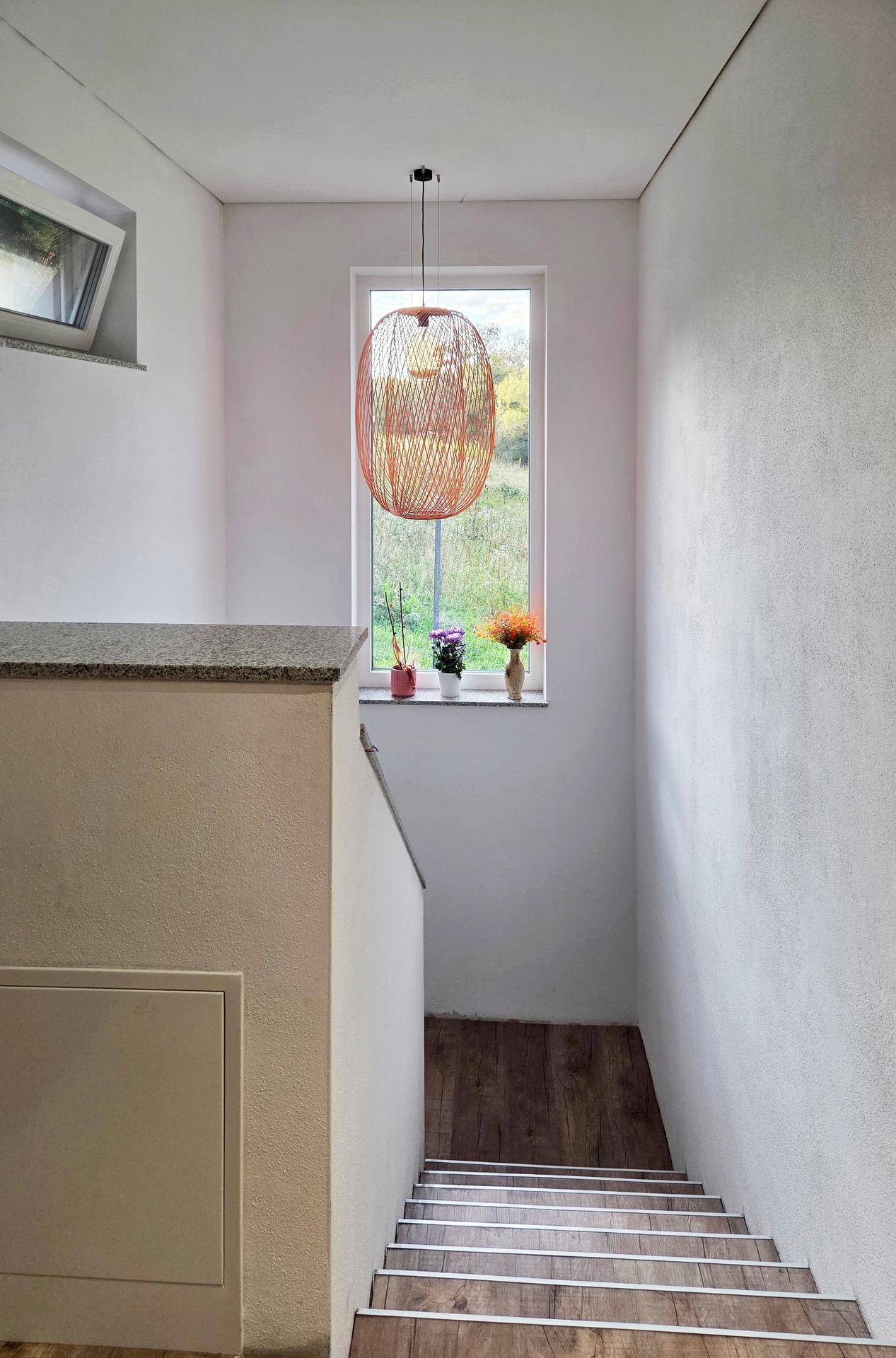 Heller Treppenaufgang mit großem Fenster, das viel Tageslicht hereinlässt und eine moderne Pendelleuchte.