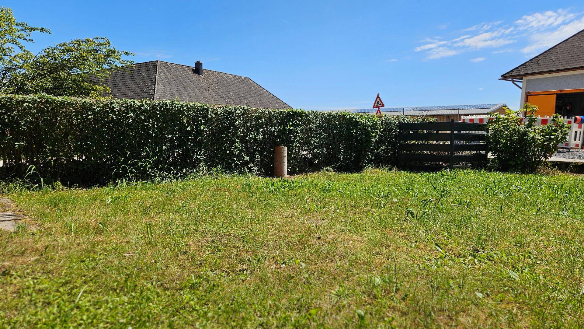 Grüner Gartenbereich mit Rasenfläche und einer hohen Hecke, umgeben von Häusern.